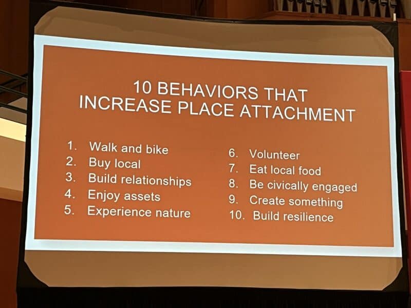 Photo by Becky McCray. Slide by Melody Warnick Slide with text. It says, "10 behaviors that increase place attachment. Walk and bike. Buy local. Build relationships. Enjoy assets. Experience nature. Volunteer. Eat local food. Be civically engaged. Create something. Build resilience."