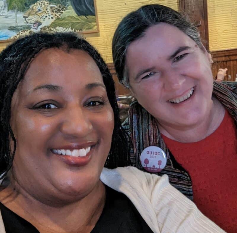 Photo by Cheryl Lawson Two women smiling in a selfie. One is wearing a pinback button that says, "OU IQC 2023"
