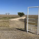 Wide view of a prairie landscape with a walk-through gate in a fence