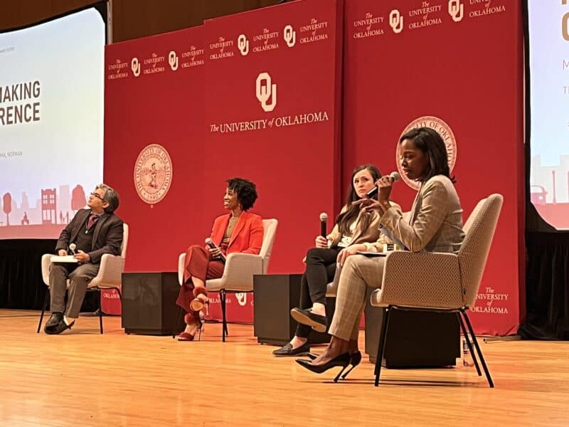 Photo by Becky McCray A diverse panel of people seated in chairs on a stage, all holding microphones. One woman is leading the discussion.